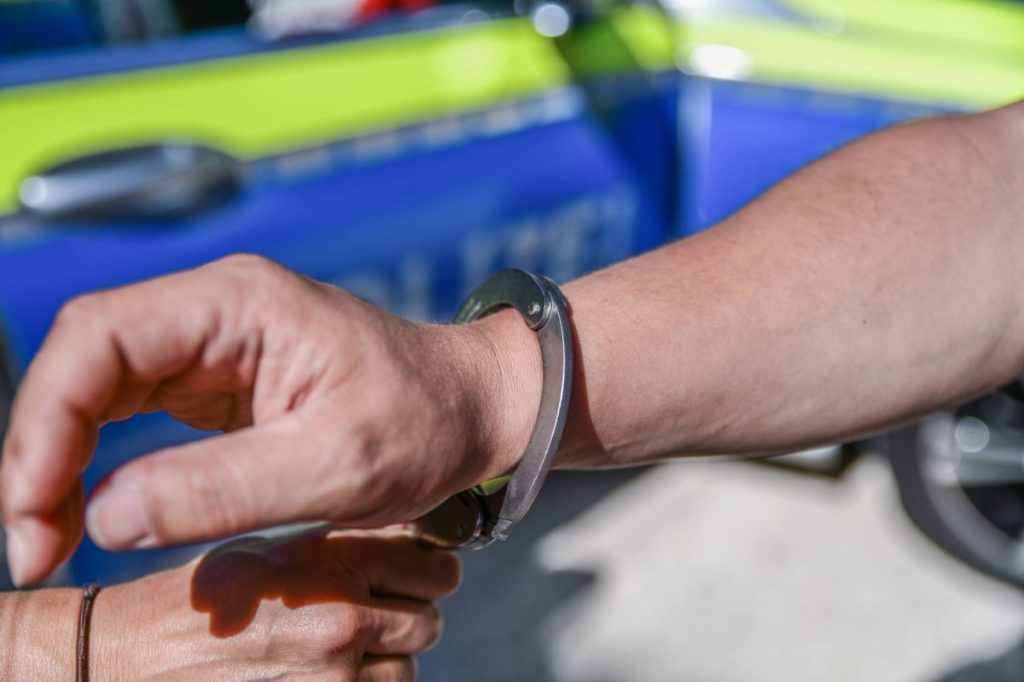 Mann werden Handschellen vor Polizeiauto angelegt 