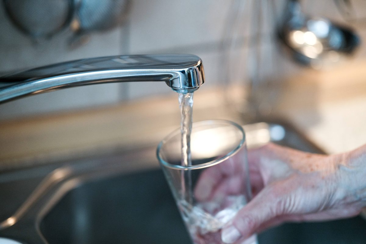 Frau hält Glas unter den Wasserhahn