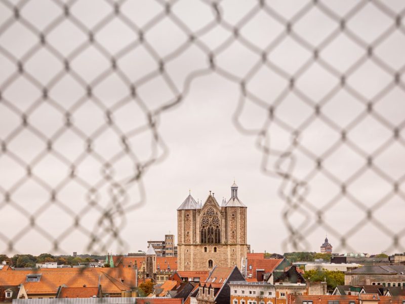 Der Braunschweiger Dom ist bei trübem Wetter durch ein Loch in einem Zaun am Horizont zu sehen.