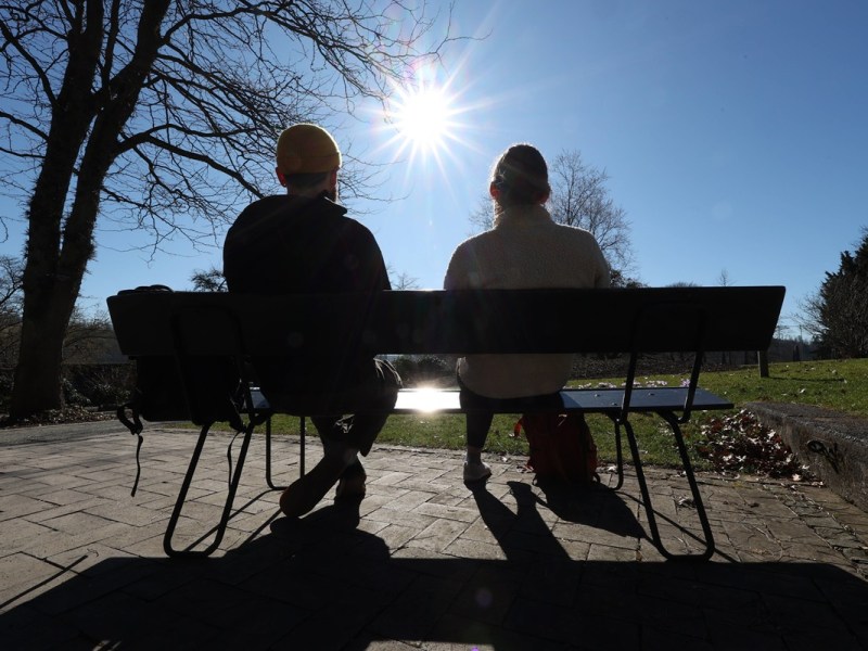 Zwei Menschen sitzen auf einer Parkbank und geniessen genießen die Sonne.