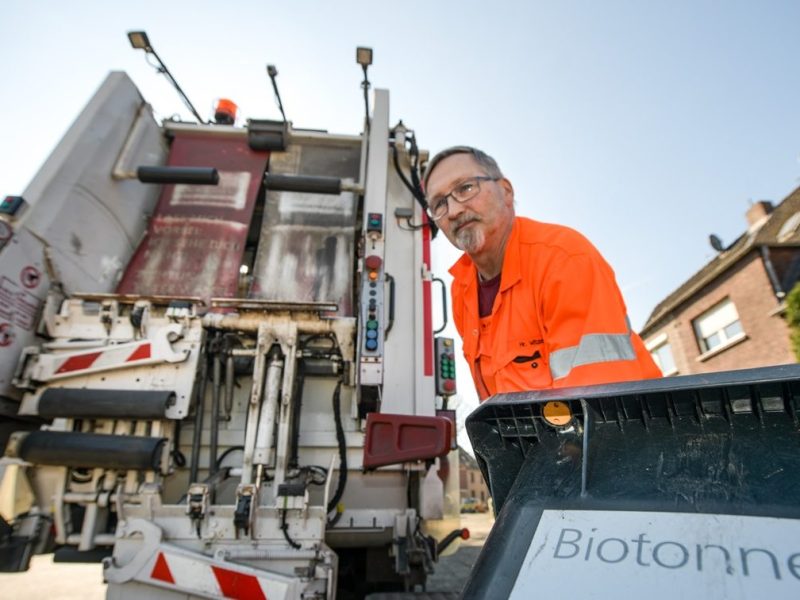 Mitarbeiter während der Müllentsorgung einer Biotonne vor dem Fahrzeug