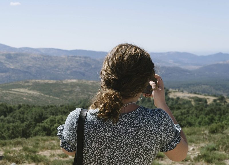 Rückansicht einer jungen Frau, die mit ihrem Mobiltelefon Fotos von der Landschaft macht.